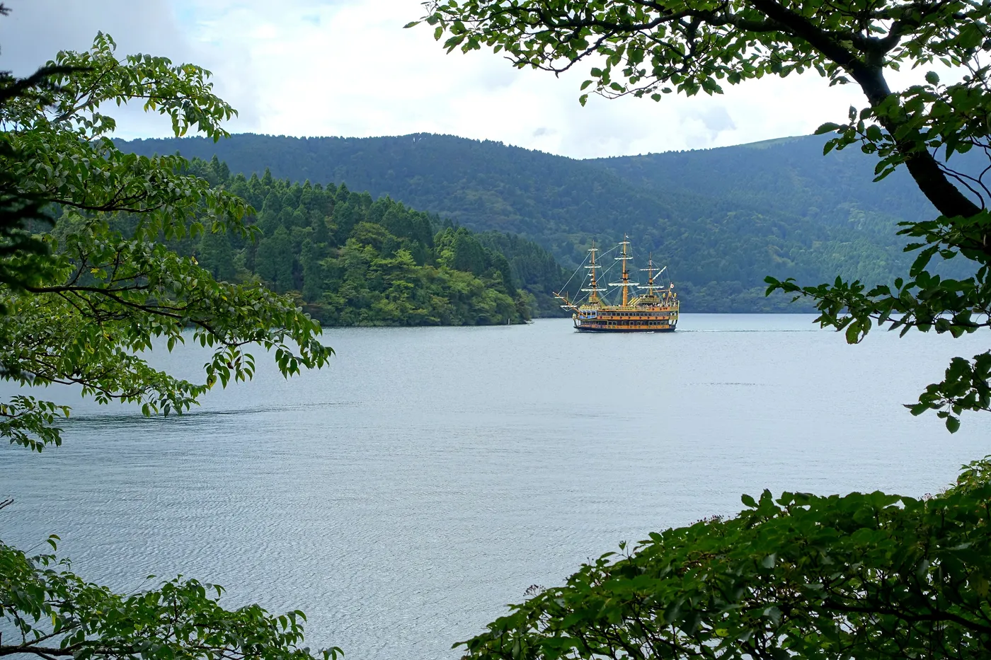 A three-masted pirate ship crossing Lake Ashi below forested hills