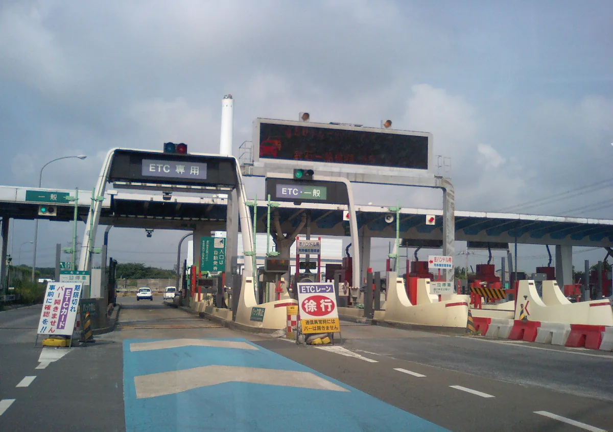 A toll plaza with an ETC専用 gantry and a shared ETC・一般 gantry, and a yellow sign telling drivers to slow down