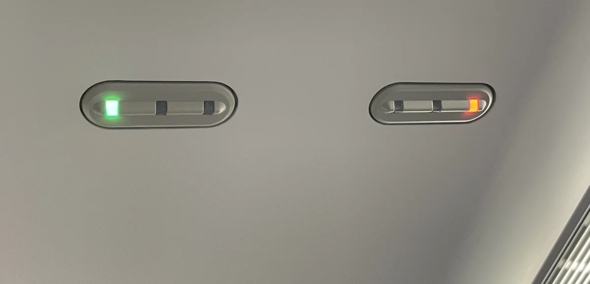 Two overhead seat indicator lamps on a train ceiling, one lit green and one lit red
